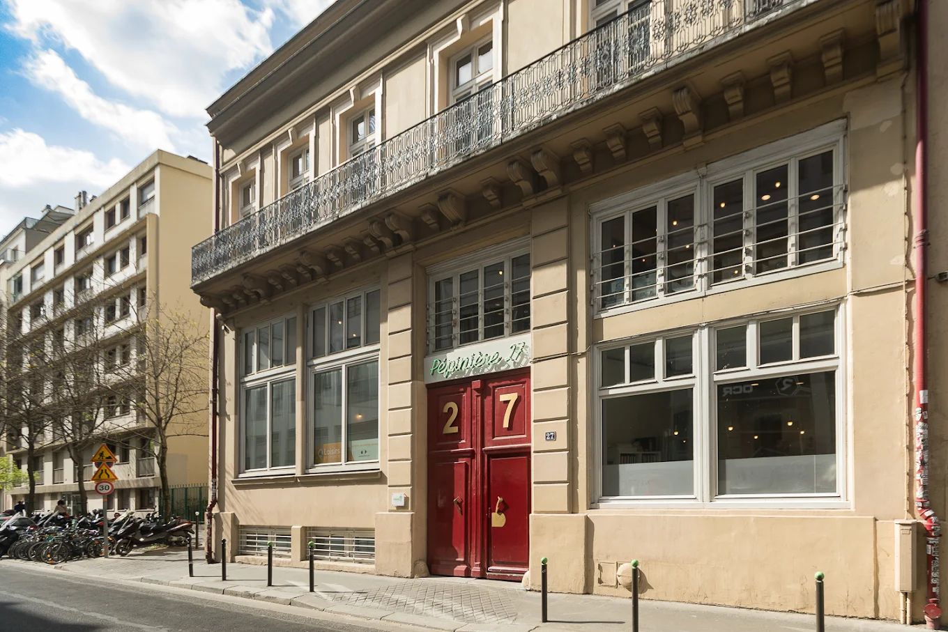 La façade du 27 rue du Chemin Vert, sa grande porte rouge et son enseigne « Pépinière 27 ».