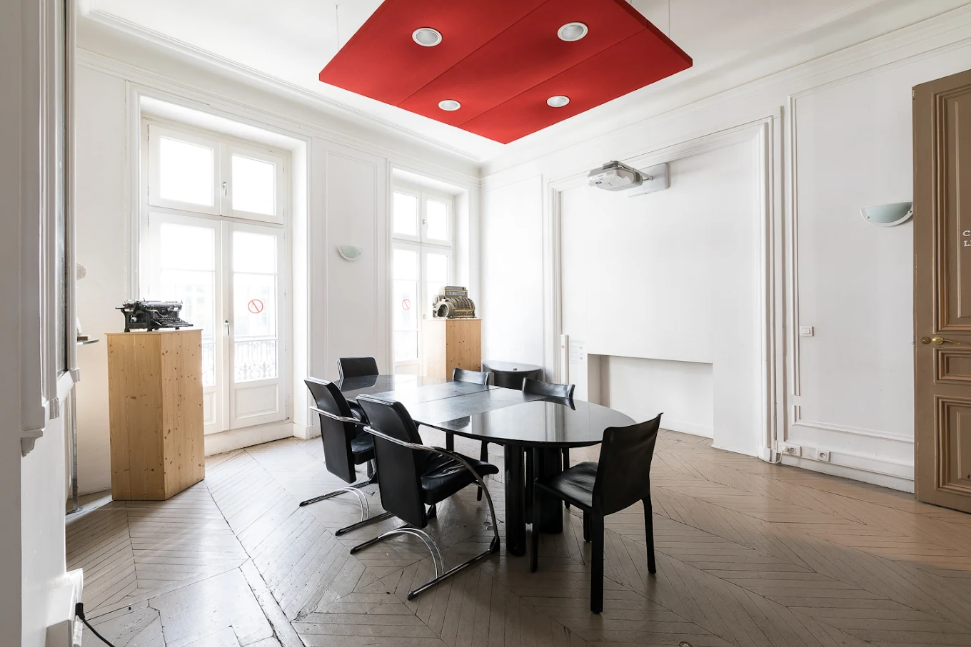 Une salle de réunion aux moulures blanches, parquet en point de Hongrie et plafond acoustique rouge.